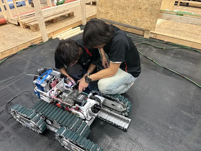 Two team members working on TUBer's electronics in the arena